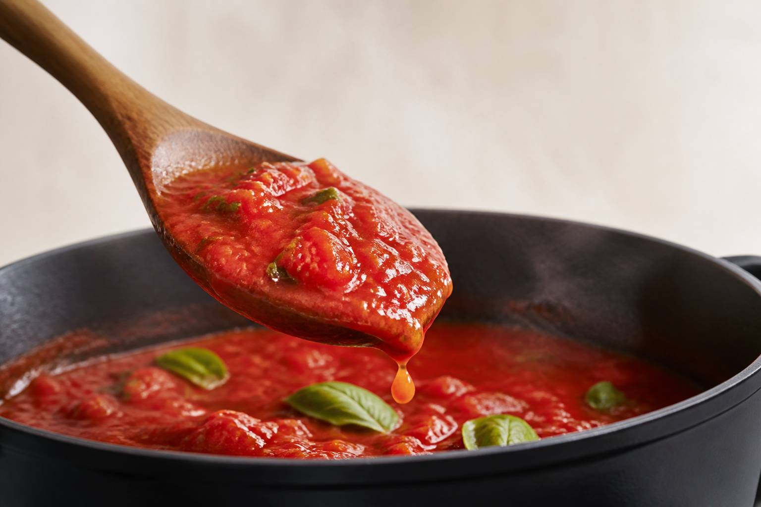 Cuillère en bois soulevant une sauce tomate maison avec des feuilles de basilic