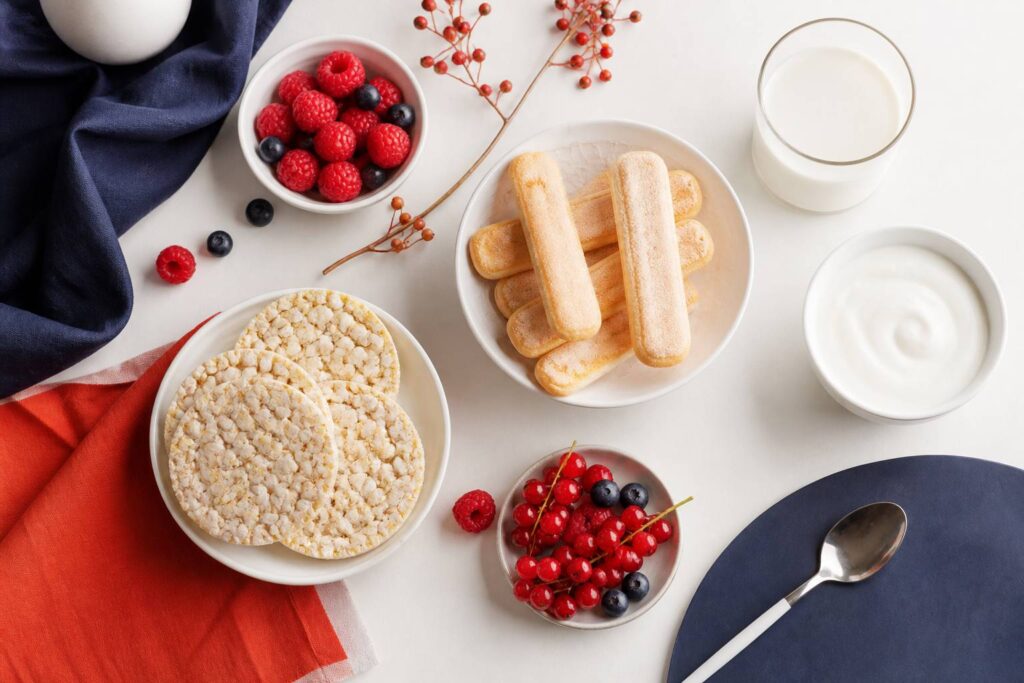 Flat-lay de biscuits secs génériques avec boudoirs, galettes de riz, yaourt nature et fruits rouges